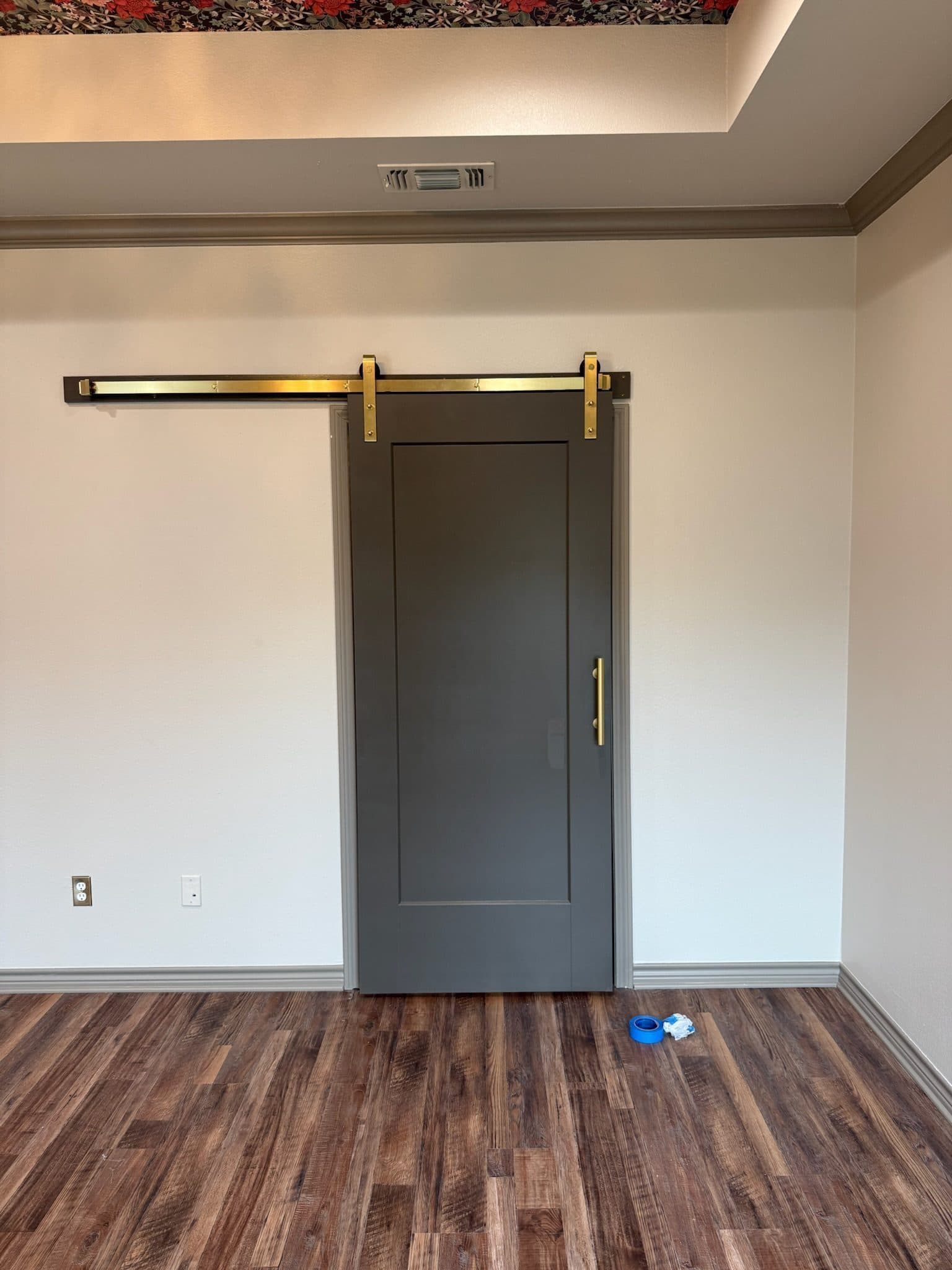 Gray barn door on brass hardware leading into primary bath
