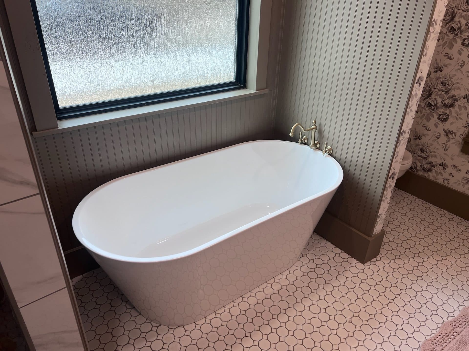 Freestanding soaking tub on pink penny tile with beadboard wainscot