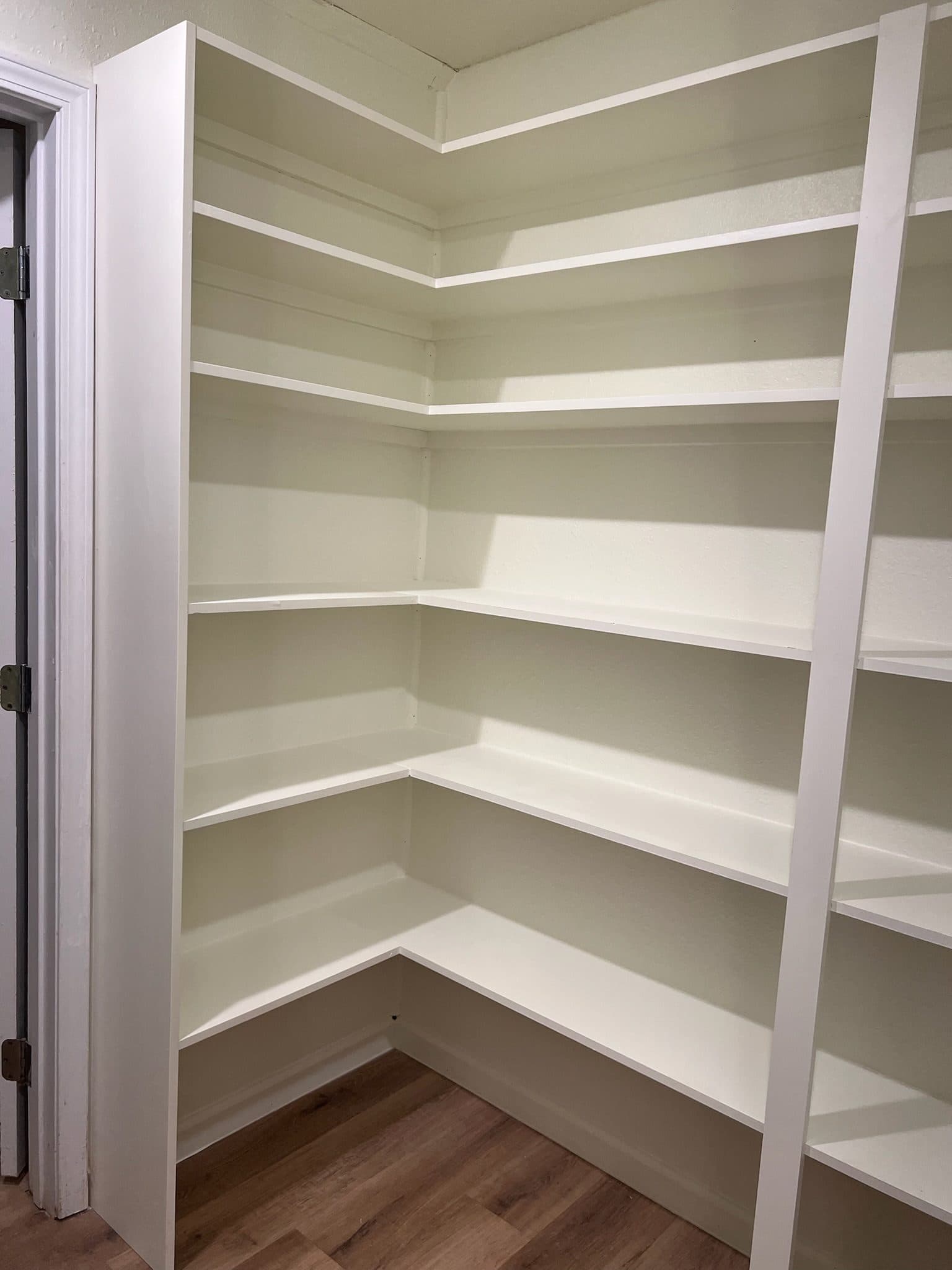 Newly built walk-in pantry with white wrap-around corner shelving
